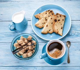 Cup of coffee, milk jug, cane sugar cubes and fruit-cake.