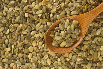 Macro background of pumpkin seeds and a wooden spoon