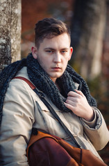 young guy in a warm cap and a jacket with a scarf on the neck, trousers and rubber boots walks alone in the Carpathian mountains with a camera, a tripod and a backpack on his shoulders