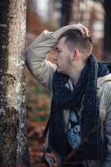 young guy in a warm cap and a jacket with a scarf on the neck, trousers and rubber boots walks alone in the Carpathian mountains with a camera, a tripod and a backpack on his shoulders