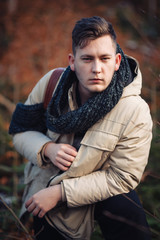 young guy in a warm cap and a jacket with a scarf on the neck, trousers and rubber boots walks alone in the Carpathian mountains with a camera, a tripod and a backpack on his shoulders