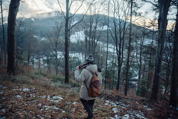 young guy in a warm cap and a jacket with a scarf on the neck, trousers and rubber boots walks alone in the Carpathian mountains with a camera, a tripod and a backpack on his shoulders