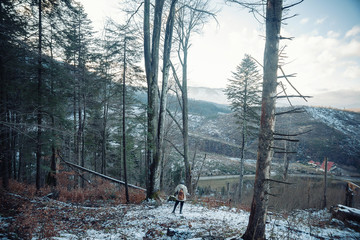 young guy in a warm cap and a jacket with a scarf on the neck, trousers and rubber boots walks alone in the Carpathian mountains with a camera, a tripod and a backpack on his shoulders