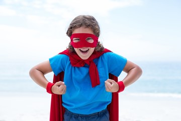 Cheerful boy in superhero costume flexing muscles at sea shore