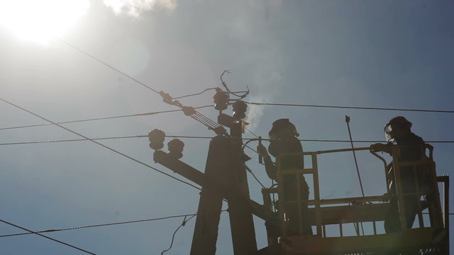 Two electricians repairing electrical wires on a pole