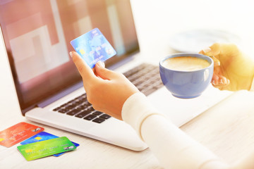 E-commerce concept. Woman with credit card, laptop and cup of coffee, close up