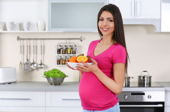 Pregnant woman holding plate with fresh juicy fruits in the kitchen