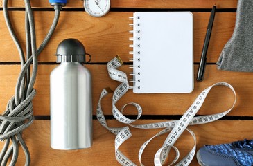 Athlete's set with female clothing, equipment, bottle of water and notebook on wooden background