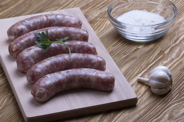 Raw sausages, salt and garlic on wooden table