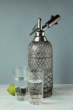 
 Soda water. Siphon and two glasses with soda water on a gray-blue background