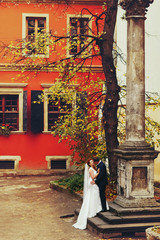 grom hugging bride with red hair outdoors background red wall  L