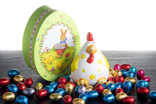 Ovetti  di cioccolato  nella  stagnola colorata con gallina in ceramica  e scatola verde decorata  a forma di uovo su un tavolo