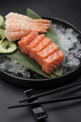 Salmon sashimi on a bamboo list and ice over black background
