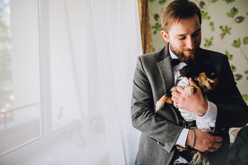 Groom with a beard holding and playing with a small dog