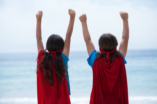 Siblings standing with arms raised at sea shore