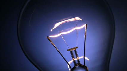 Close up of the filament of an electric light bulb glowing on and off. Blue background.