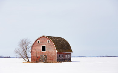 An old weathered red barn with hayloft in a barren countryside winter landscape