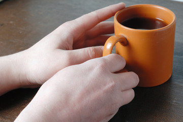 Males hand holding orange cup of tea