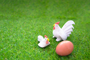 Ceramic chickens and eggs on grass, doll / Still life of Ceramic hen and cock chicken with egg on green grass