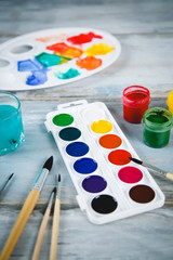 Naklejka premium Set of watercolor paints, brushes for painting and palette on old vintage wooden background top view