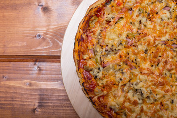Flat lay Italian pizza with ham and mushrooms on a wooden round tray on wooden table top view