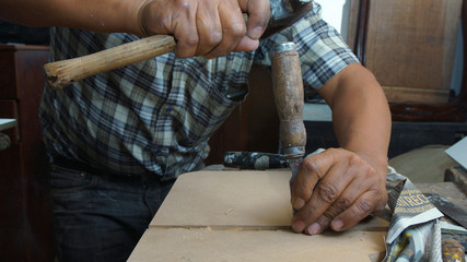 Carpenter hitting a chisel with a hammer modeling a wooden board on his desk