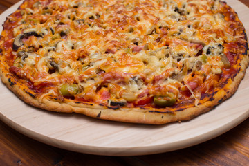 Italian pizza with ham and mushrooms on a wooden board on natural wooden table