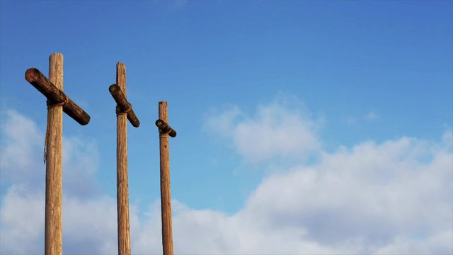 Three rugged wooden crosses are backed by clouds moving in a deep blue sky. Looping.