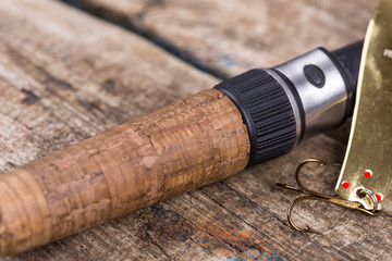 handle of fishing rod with lure on wooden