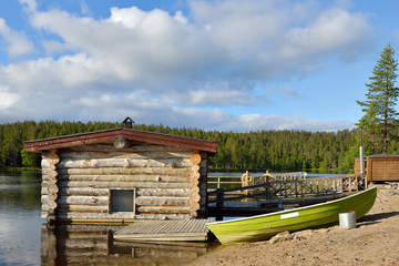 Log sauna on shore of lake. Landscape with boat