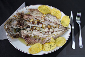 Close up of grilled fish emplatado with garlic, oil and potatoes.