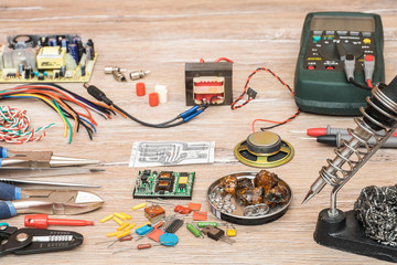 Tools for the designing and repair of electronic devices. Soldering iron, tools, electronic components, wire, devices and multimeter on a wooden table.
