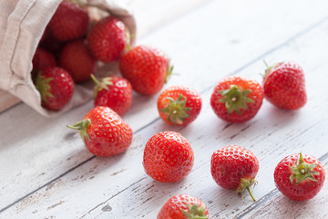 Fresh strawberries spilling out of a hessian bag on its side.