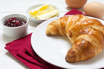 Sunday breakfast with croissant, jam and eggs, red napkin on white wood