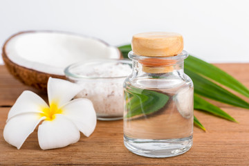 coconut oil in a bottle, background is a half of coconut on the wooden table, isolated