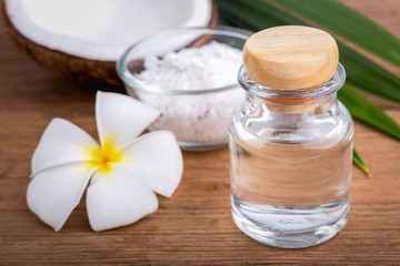 coconut oil in a bottle, background is a half of coconut and leaf on the wooden table