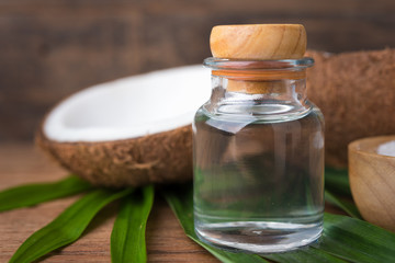 coconut oil in a bottle, background is a half of coconut and leaf on the wooden table