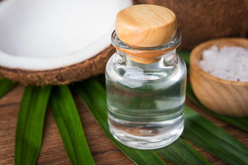 coconut oil in a bottle, background is a half of coconut and leaf on the wooden table