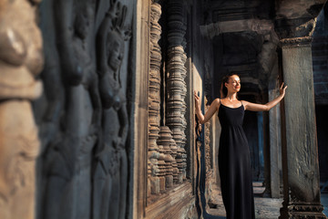 Naklejka premium Cambodia Tourist Attraction. Happy Beautiful Religious Young Woman Relaxing In Corridor At Prasat Angkor Khmer Wat Temple, Siem Reap. Famous Landmark, Travel Destination. Harmony, Tranquility Concept