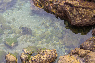 Crystal blue waters along rocks with seaweed
