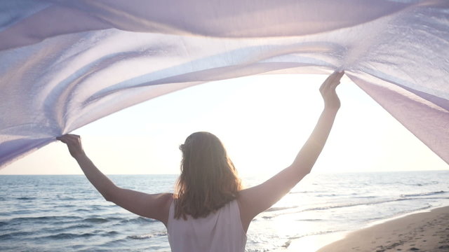 Beautiful woman holding light fabric on the beach and enjoy the sunset