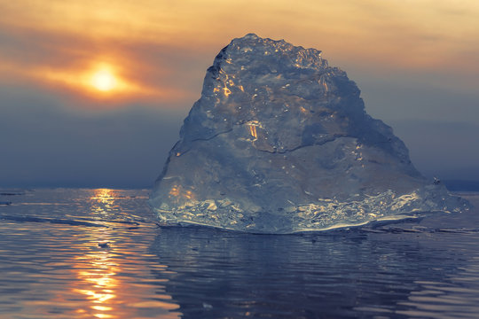 Transparent piece of ice on sunset sky background.