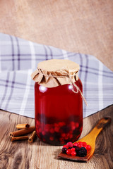 Sweet delicious compote of berries in glass jar on wooden table.