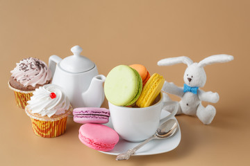 Colorful French macaroons and cup of tea on beige background