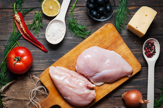 Chicken breast, wooden spoon and fresh delicious ingredients for cooking on rustic background
