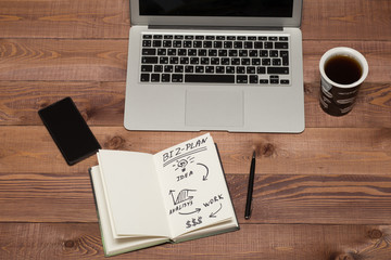 Notebook with business plan, phone, laptop. coffee cup on table