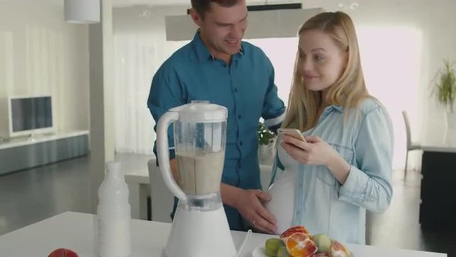 Beautiful blond pregnant woman is making a smoothie in blender and using her smartphone. Shot on RED Cinema Camera.