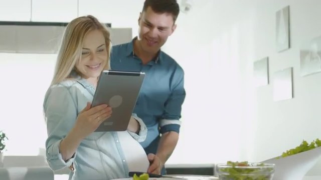 Pregnant woman is using a tablet computer while preparing healthy food in the kitchen at home. Shot on RED Cinema Camera.