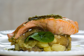 Salmon fillet, pesto and crushed potato. A restaurant prepared fish dish presented on a white plate
