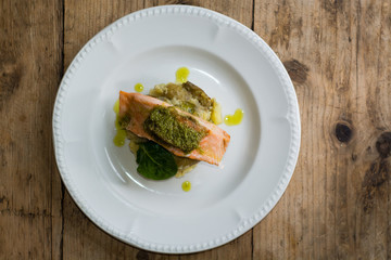 Salmon fillet, pesto and crushed potato from above. A restaurant prepared fish dish presented on a white plate
